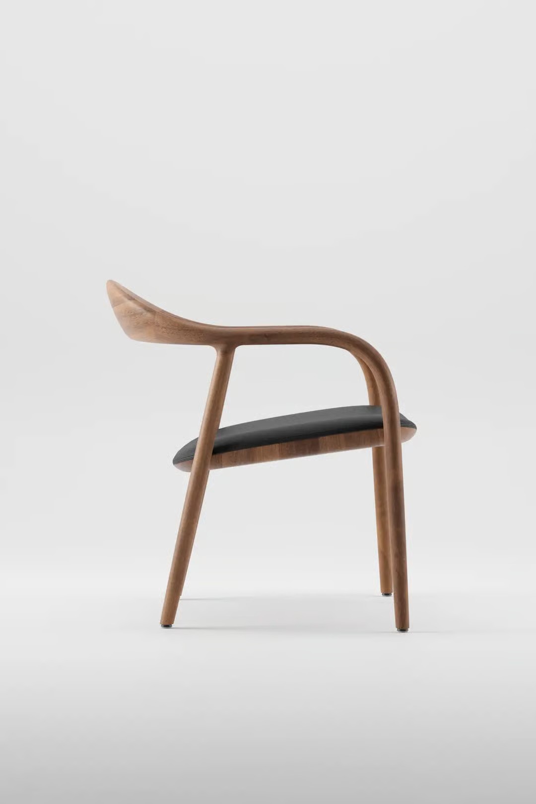 Silla de diseño, marca exclusiva europea, minimalista con estructura de madera curvada y asiento negro, fotografiada de perfil sobre fondo blanco.